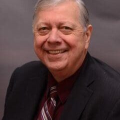 Smiling elderly man in a dark suit and maroon tie.